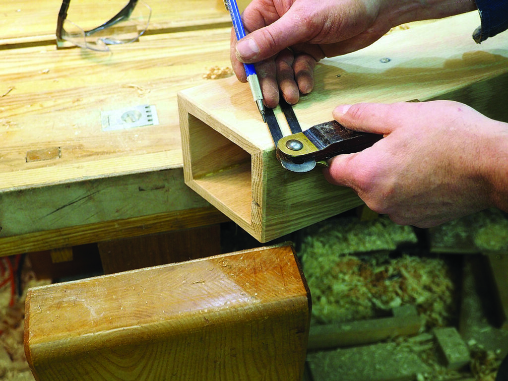 Woodworker measuring wooden joint with caliper and pencil.