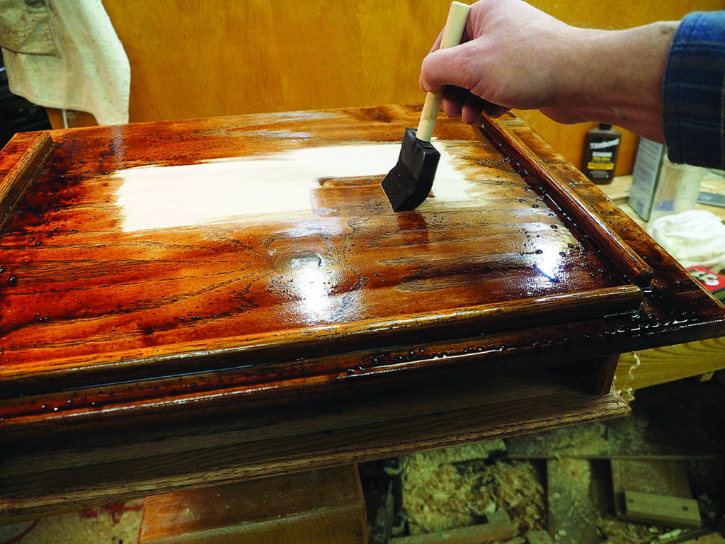 Hand applying varnish to wooden cabinet surface
