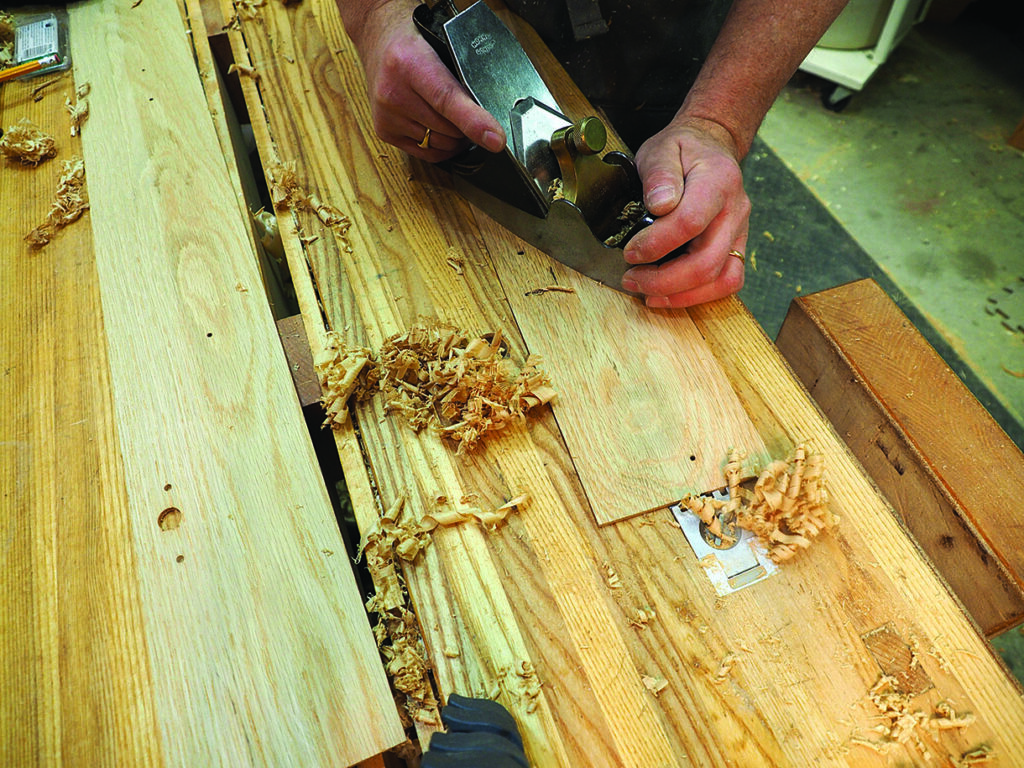 Carpenter smoothing wood with hand plane tool.