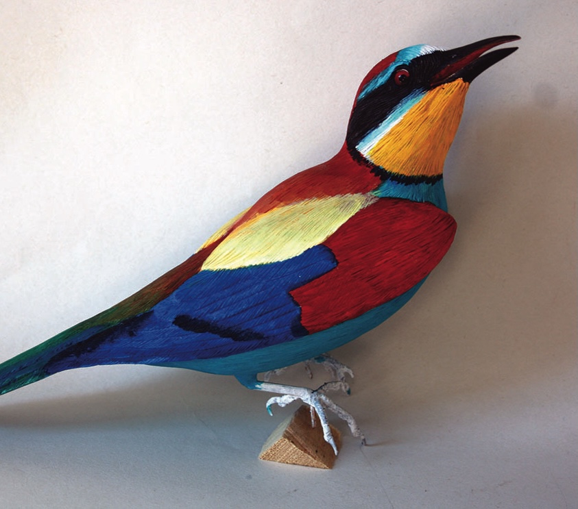 Colourful paper bird sculpture on wooden base.