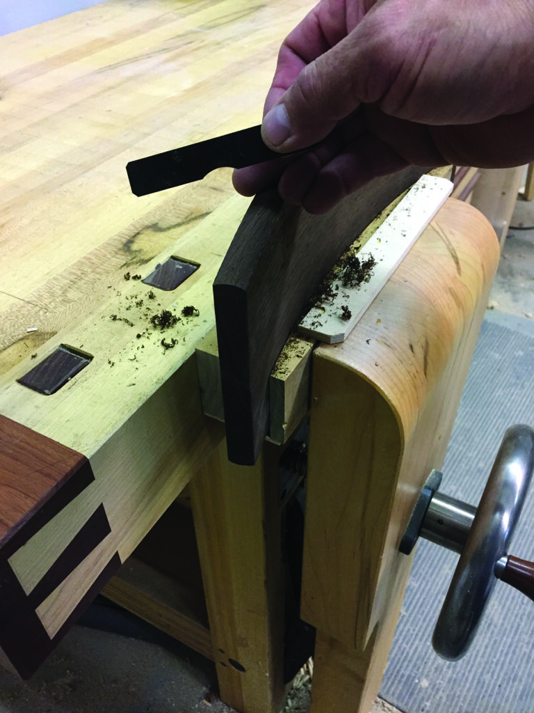 Carpenter using scraper on wood joint at workbench.