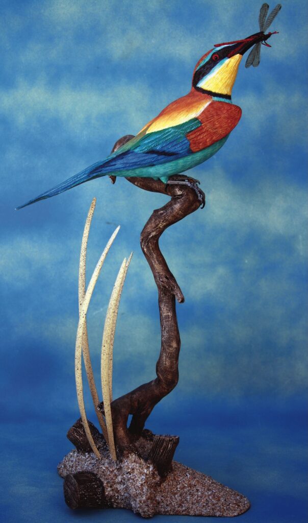 Colourful bird sculpture with dragonfly in beak.