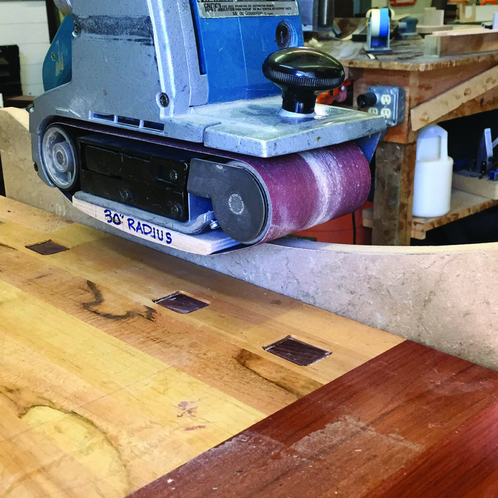 Belt sander shaping wood with 30-degree radius template.