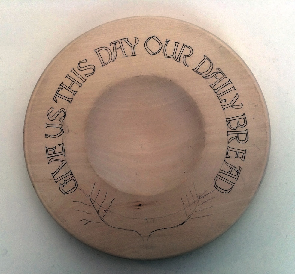 Wooden plate engraved with 'Give us our daily bread'