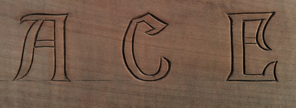 Wood carving of 'ACE' letters in serif font.