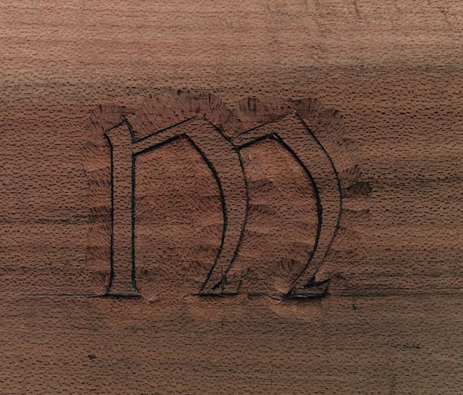 Carved calligraphy letter M on wooden surface