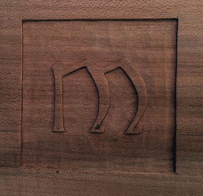 Wood carving of letter M on surface