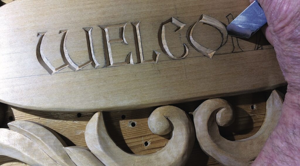 Carving wooden welcome sign with hand tools.