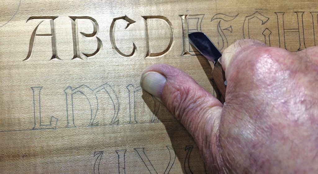 Hand carving letters into wood, creating serif font.