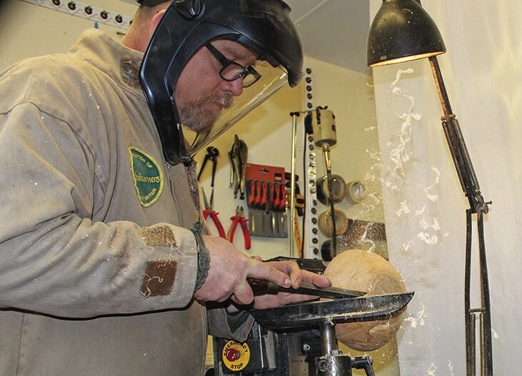 Man crafting wood on a lathe in workshop.