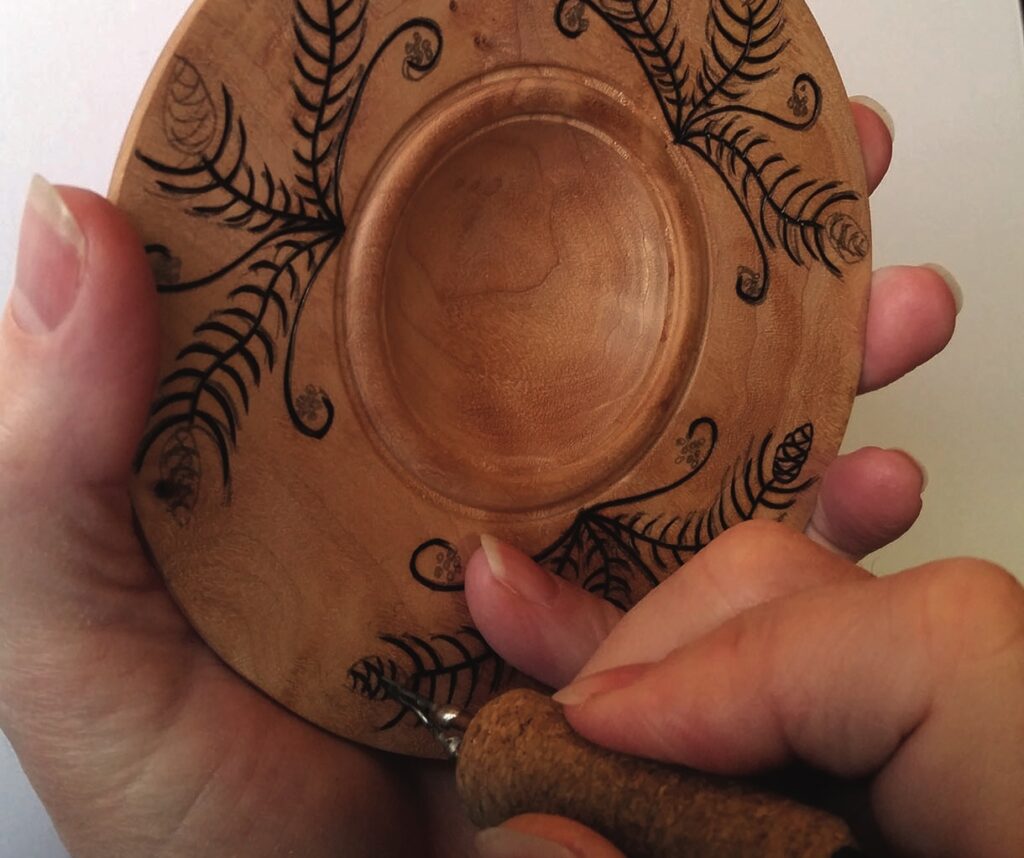Person carving intricate design on wooden plate
