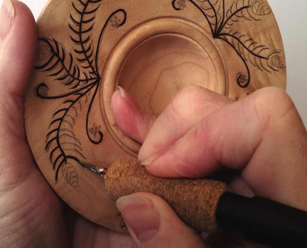 Person woodburning intricate design on a wooden plate.