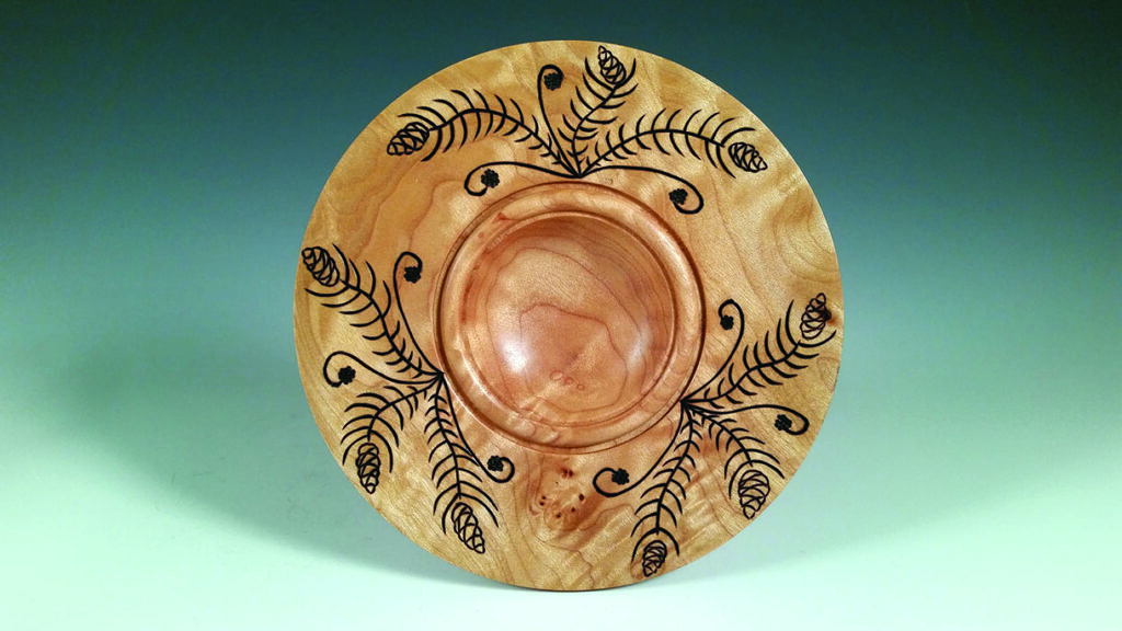 Decorative wooden plate with intricate leaf design.