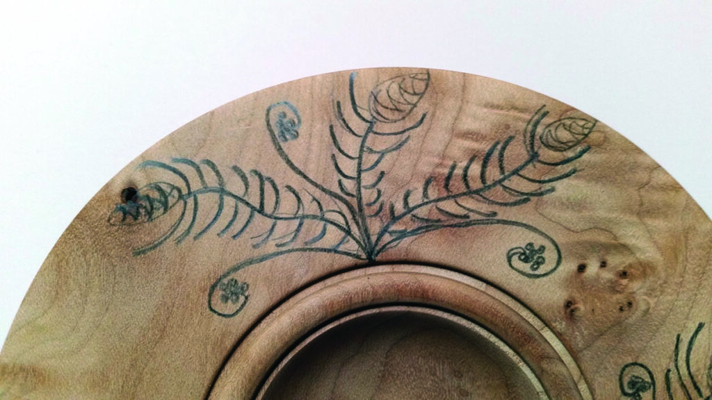 Engraved wooden plate with decorative fern pattern.