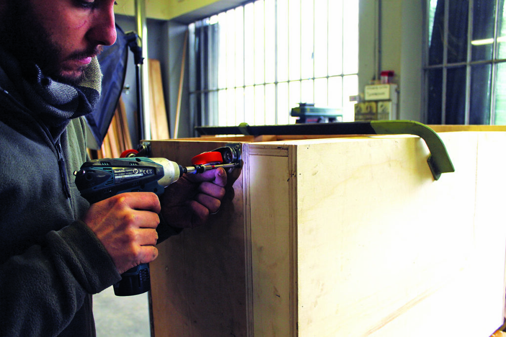 Person using drill on wooden box assembly.