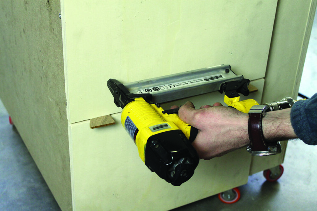 Person using a yellow nail gun on wood.