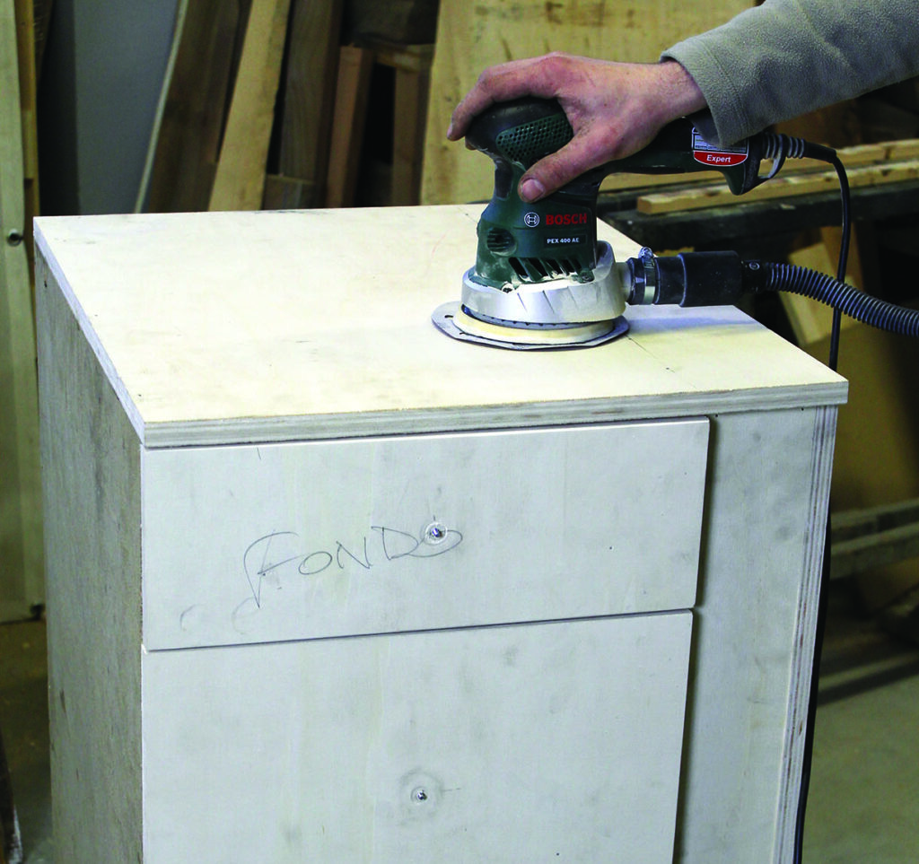 Hand sanding wooden furniture with electric sander.