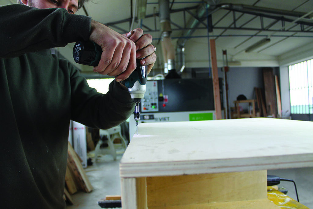 Person drilling into wooden board in workshop.