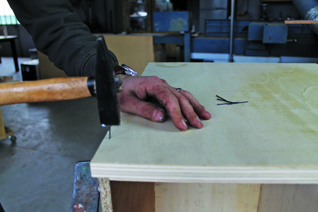 Carpenter hammering nail into wood board.