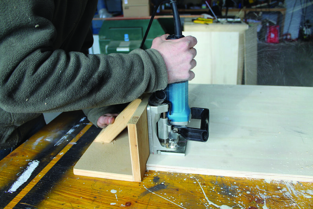 Person using router on wooden board in workshop.