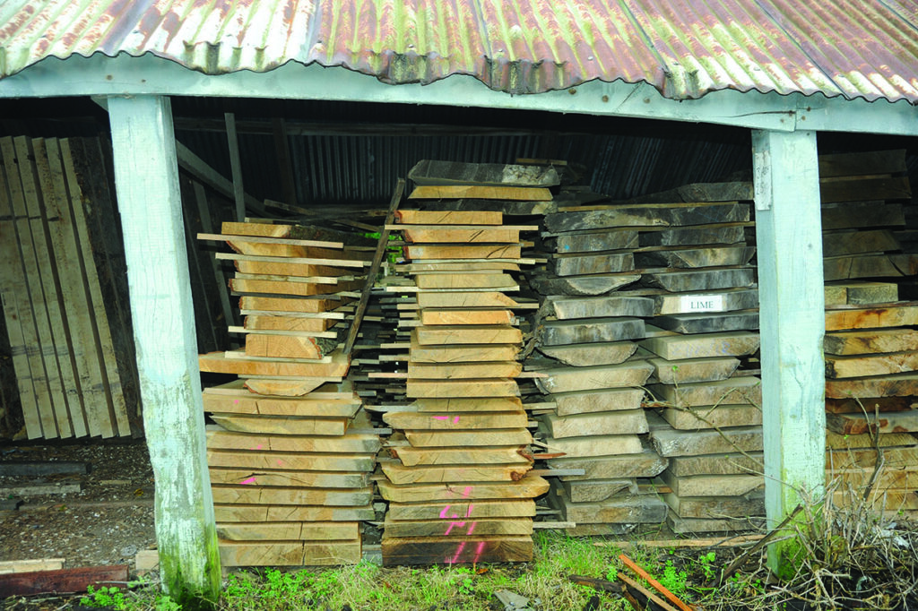 Stacked wooden planks in shed with tin roof.