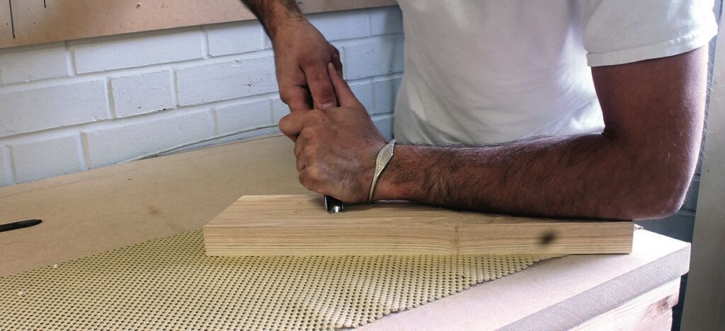 Person chiselling wood on a workbench.