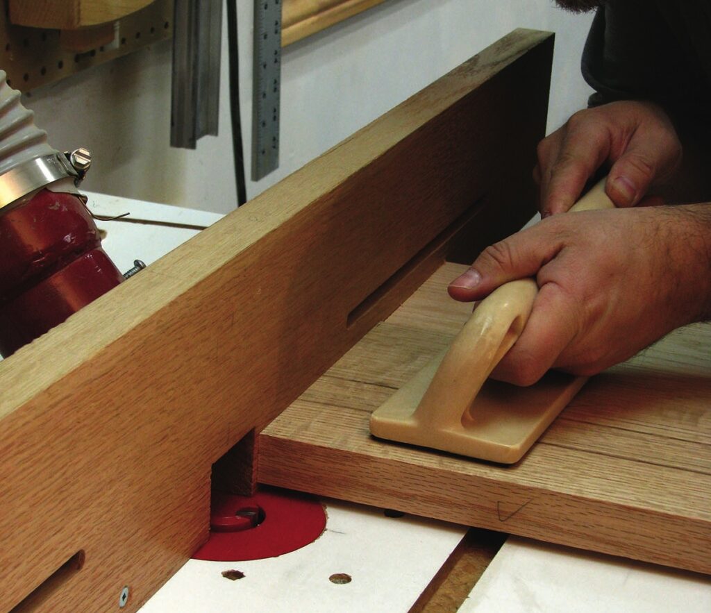 Woodworker using router table with safety push block.