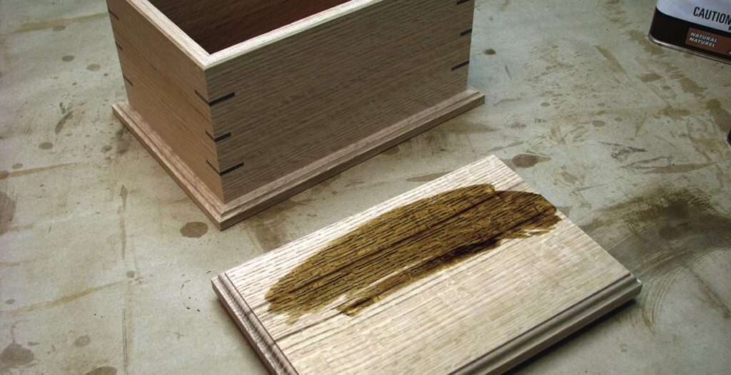 Wooden box and stained wood sample on table.