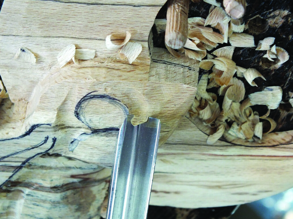 Chisel carving detailed wood pattern with shavings.