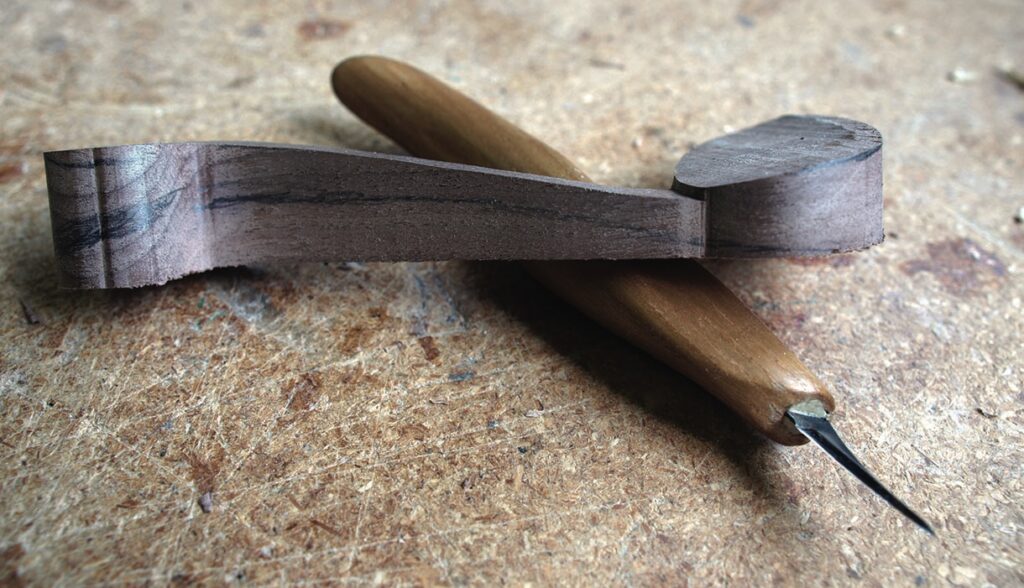 Wood carving tool and carved wooden piece on table.