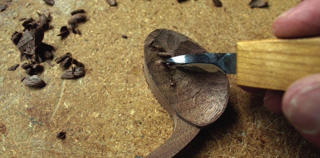 Close-up of carving a wooden spoon with a tool.