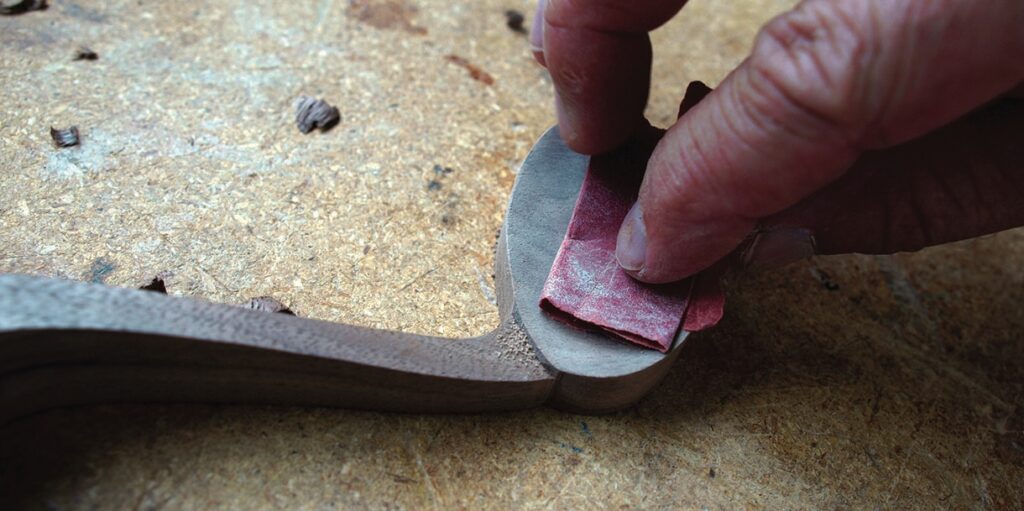 Hand sanding wooden object edge with sandpaper.