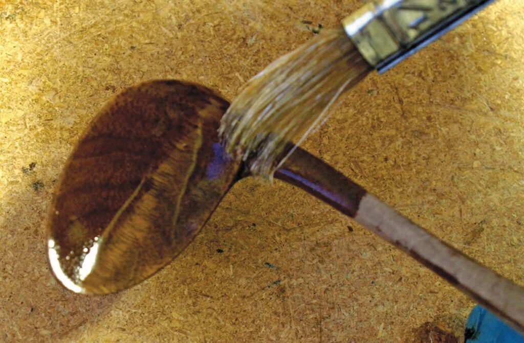 Brush applying varnish to wooden spoon