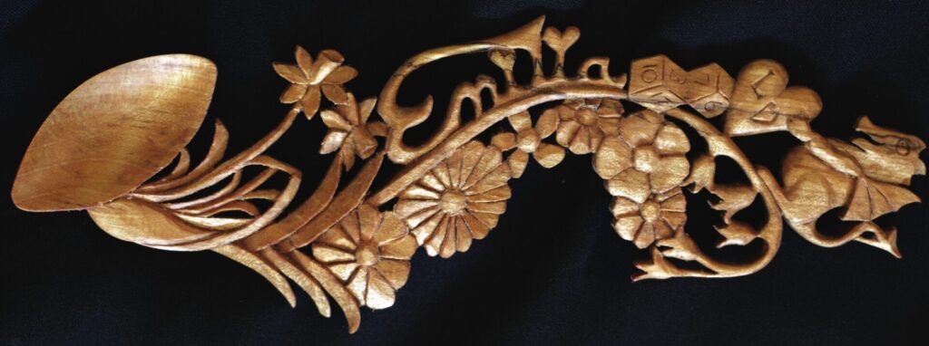 Intricate wooden lovespoon with floral and dragon carvings.