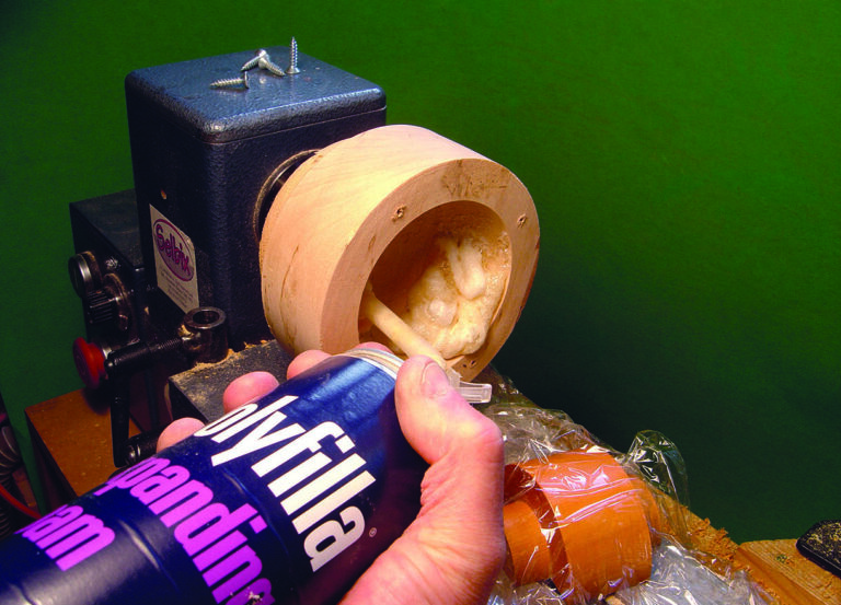 Applying expanding foam inside wooden cylinder on lathe.