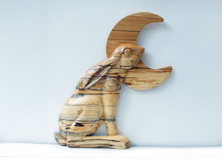 Wooden sculpture of hare leaping over crescent moon.