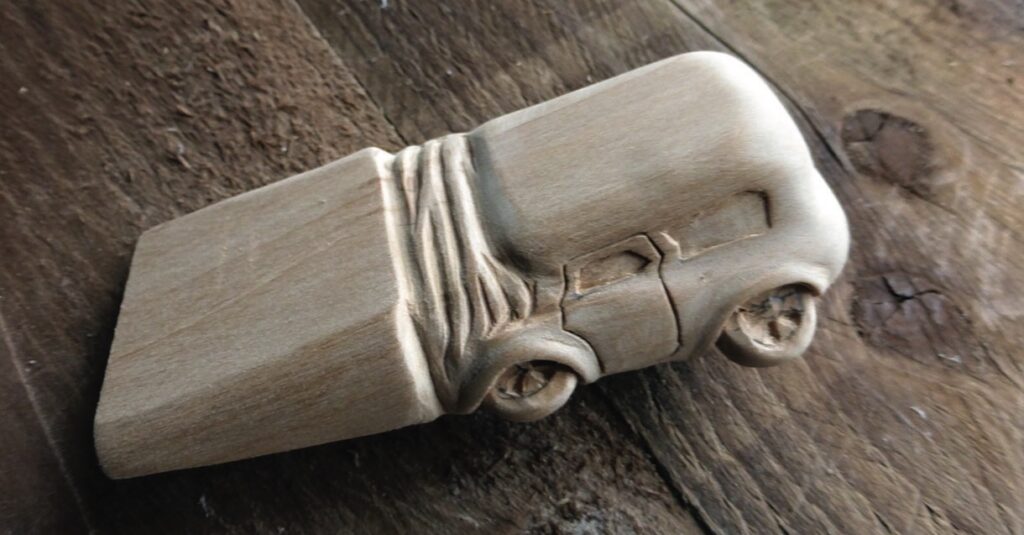 Wooden carved car doorstop on wooden surface.