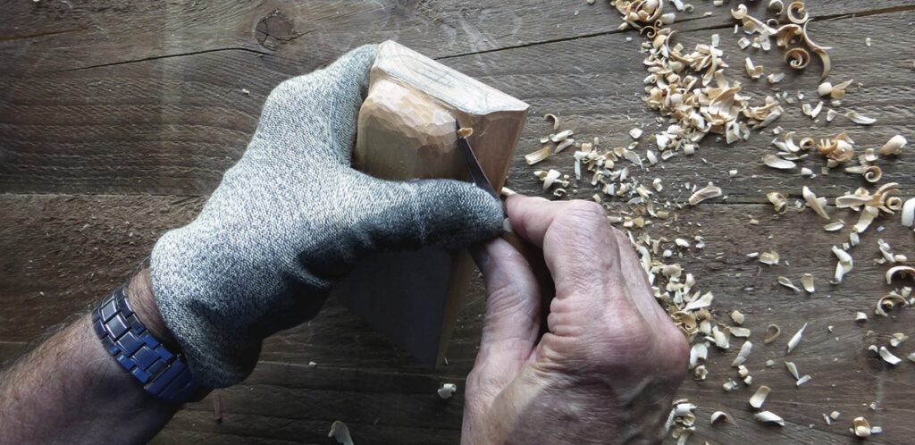 Person carving wood with gloves and tools.