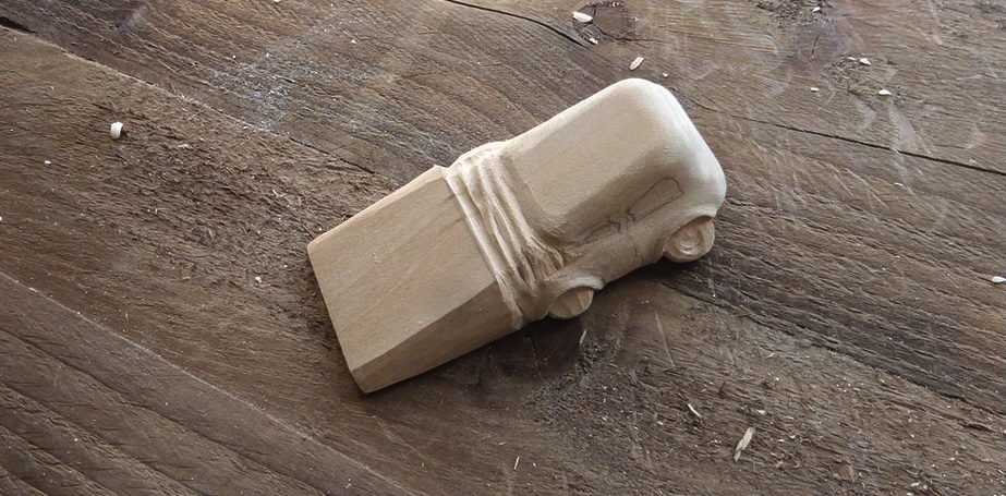 Wooden toy car carved from block on wood surface.