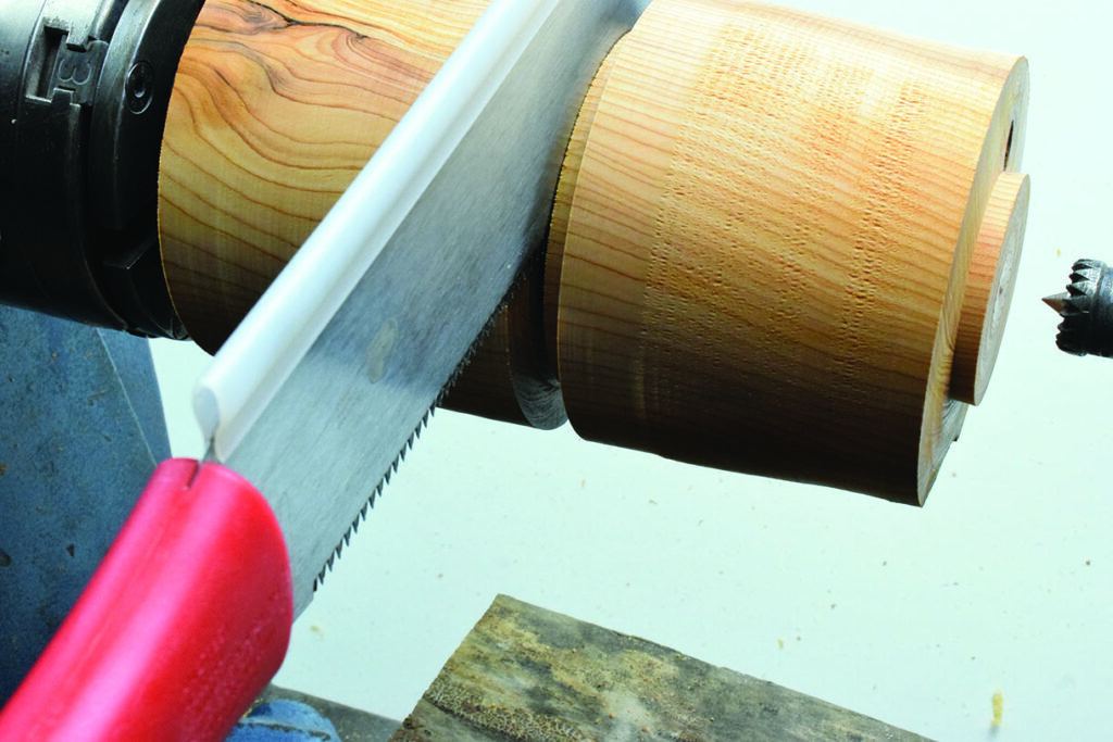 Saw cutting wooden piece on lathe machine.