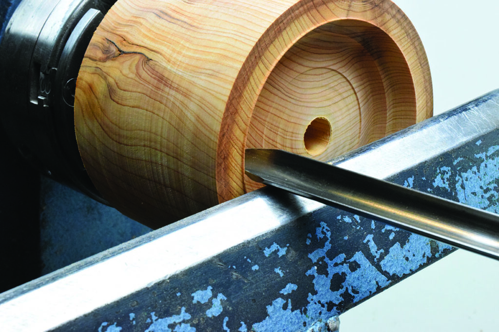 Woodturning tool carving wooden cylinder on lathe