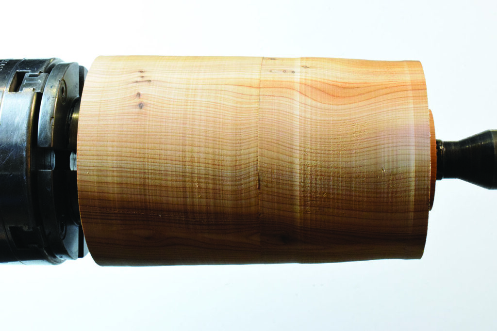 Wood lathe turning cylindrical piece in machine shop.