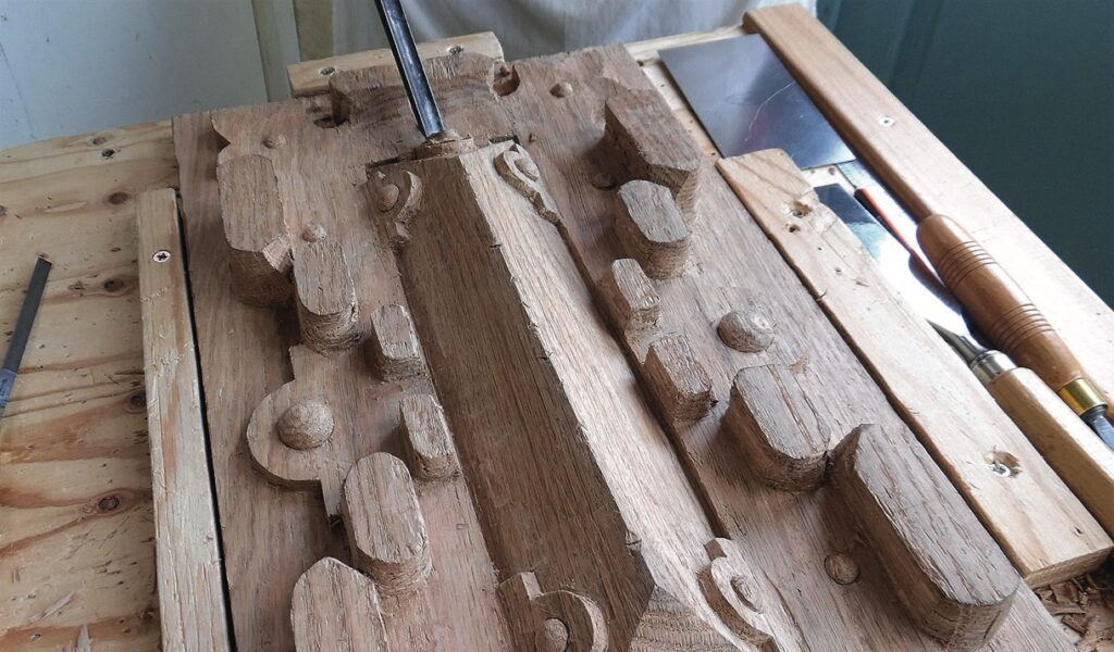 Wood carving process with chisels on wooden panel.