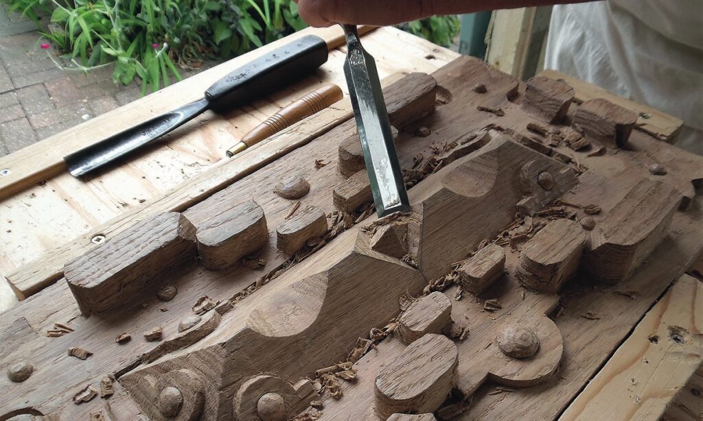 Hand carving intricate wood design with chisel.