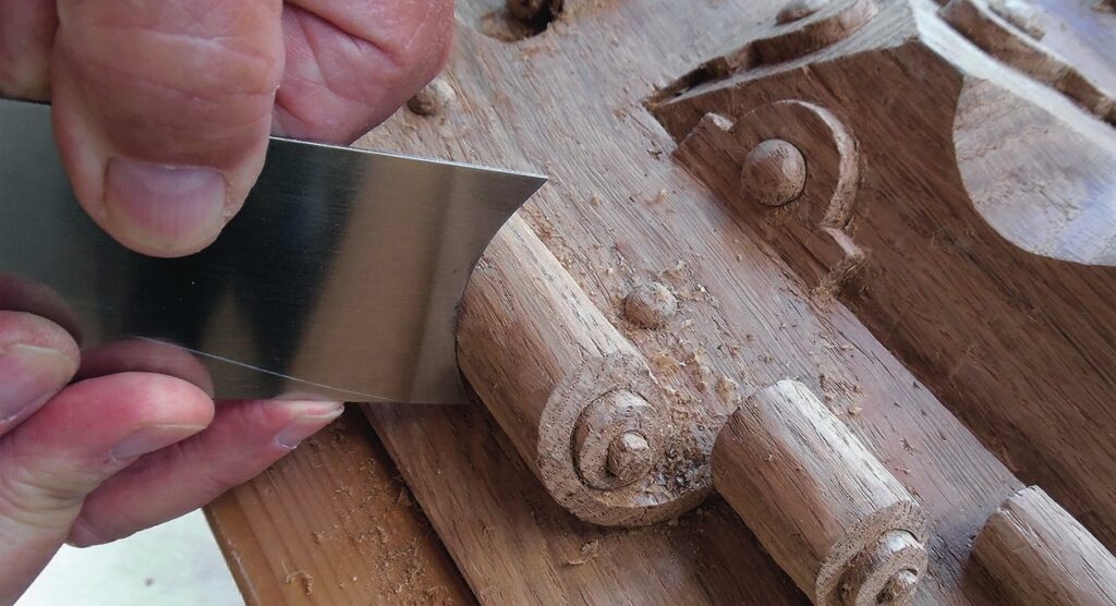 Hand carving intricate wood details with scraper tool.