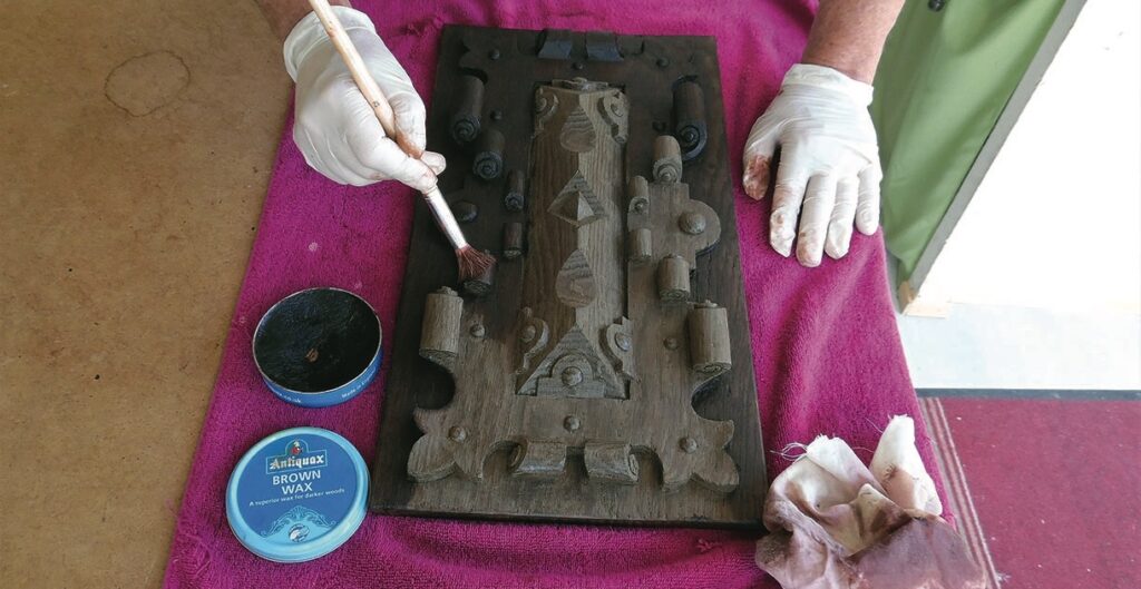 Applying wax to ornate wooden panel with brush