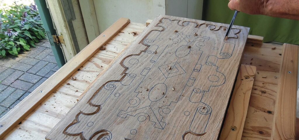 Hand carving intricate design on wooden panel.