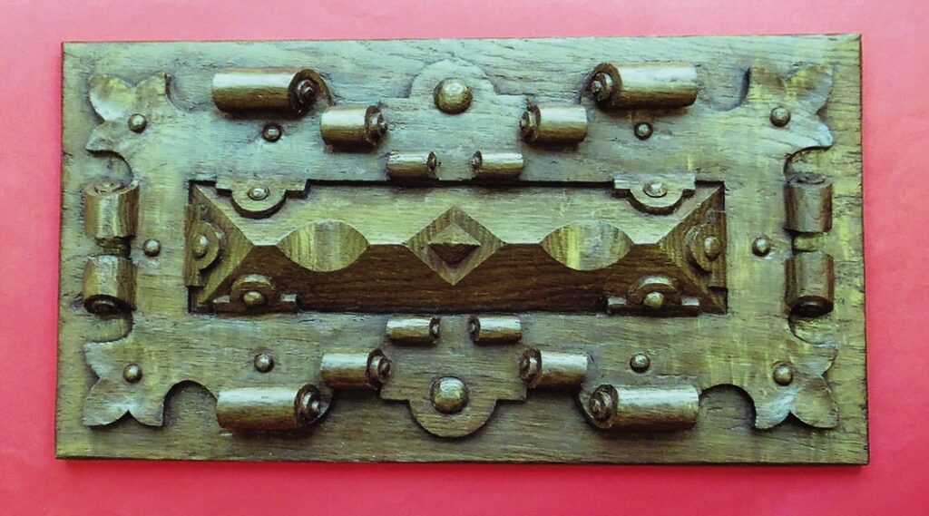 Intricately carved rectangular wooden panel on red background.