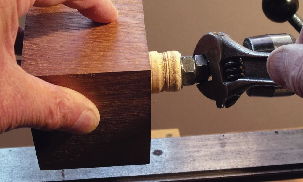 Adjustable spanner tightening wooden piece on lathe.