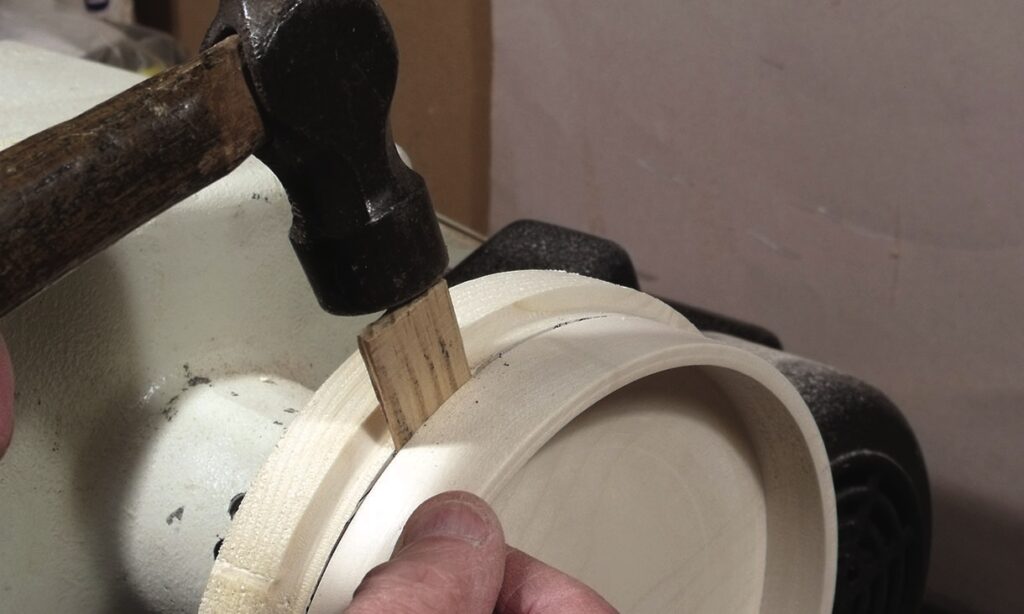 Hammer tapping chisel into wooden bowl rim
